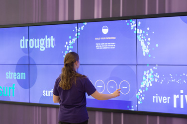 A student touching a large touchscreen on the wall.